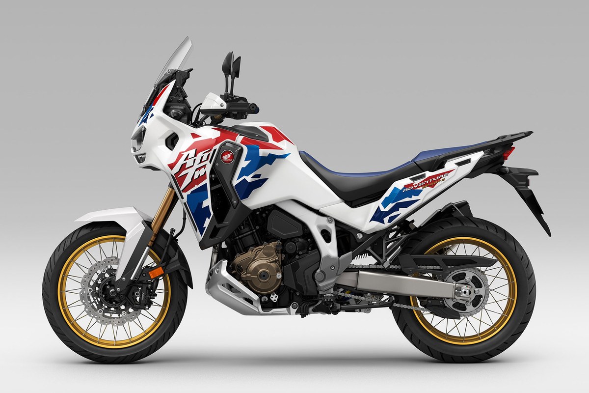 2026 Honda Africa Twin CRF1100L in white with red and blue graphics, left-side studio profile showing gold spoked wheels and a skid plate