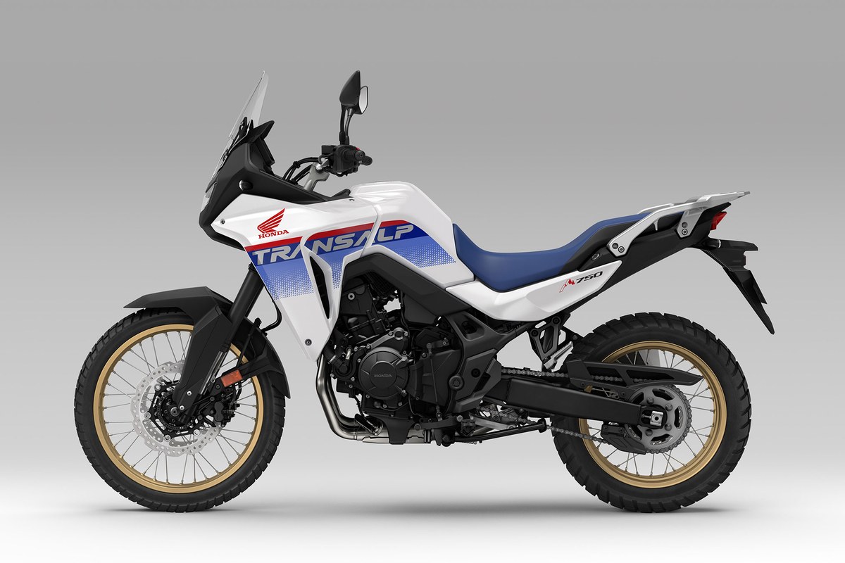 2026 Honda Transalp XL750 in white with blue and red graphics, left-side studio profile showing the gold spoked wheels and knobby tires