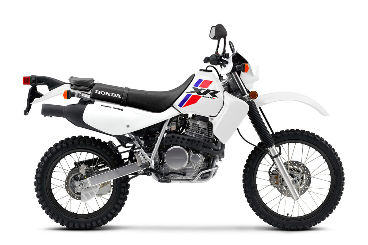 2026 Honda XR650L dual-sport motorcycle in white with red and blue graphics, left-side studio profile showing spoked wheels and long-travel forks