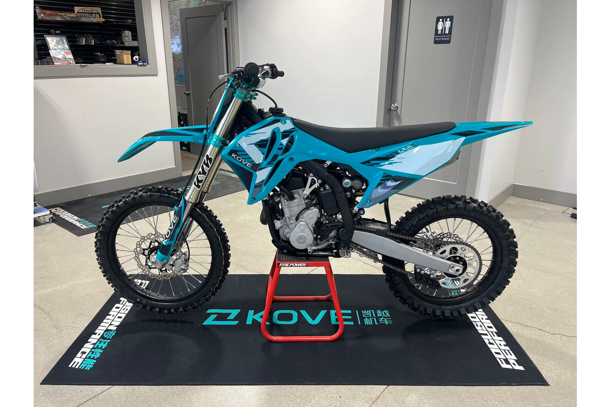 2026 Kove MX450 motocross bike in teal and white livery, left-side dealership studio profile showing KYB forks and spoked wheels