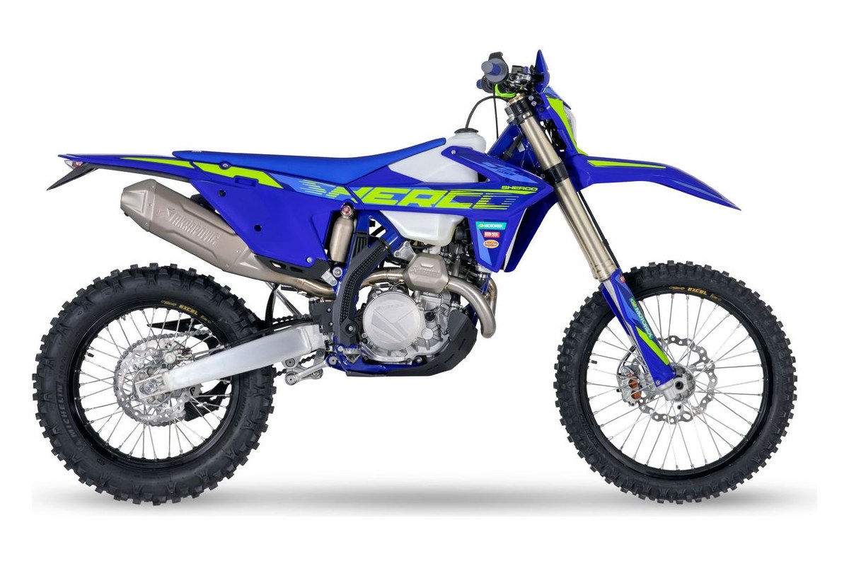 2027 Sherco 500 SEF Factory enduro motorcycle in blue and white with hi-vis green graphics, left-side studio profile showing the titanium exhaust and spoked wheels