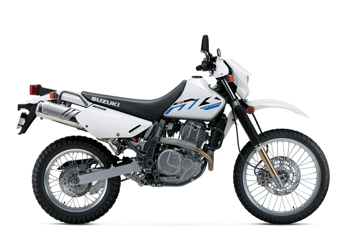 2026 Suzuki DR650S dual-sport in white with blue graphics, left-side studio profile showing the round headlight, long-travel forks and knobby tires
